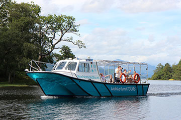 A Blue tourboat sailing between islands on Loch Lomond