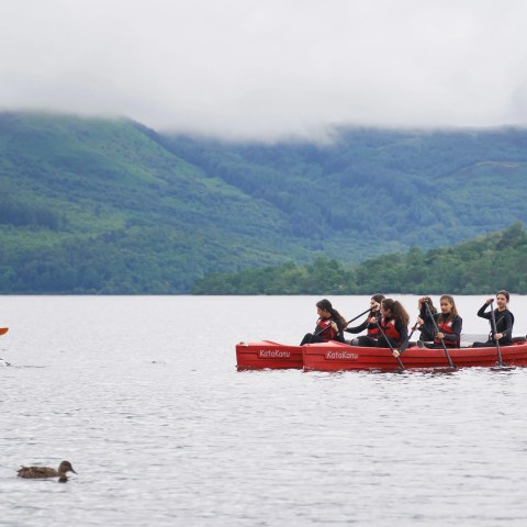 People paddling in red canoe on a lake with forested hills in background.