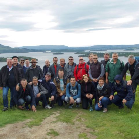 Group of people posing on a grassy hill with a lake and mountains in the background.