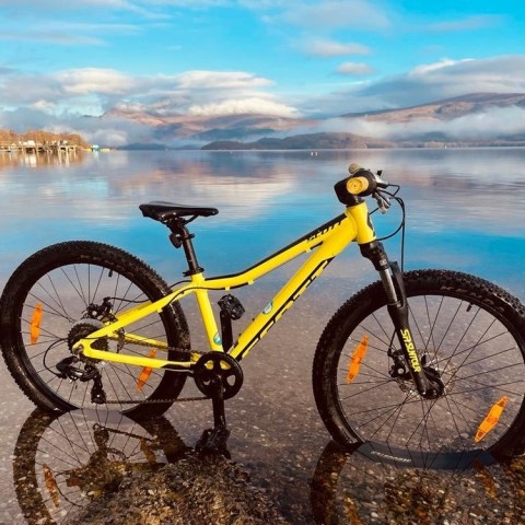 Yellow mountain bike on a lake shore with mountains and clouds in the background.