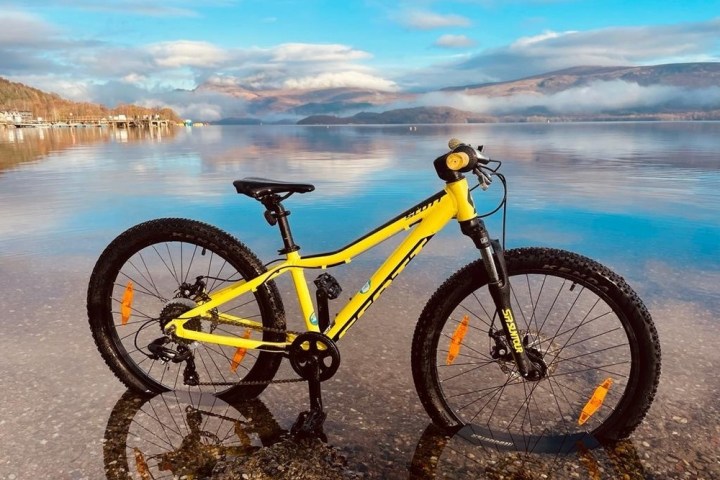 Yellow mountain bike on a lake shore with mountains and clouds in the background.
