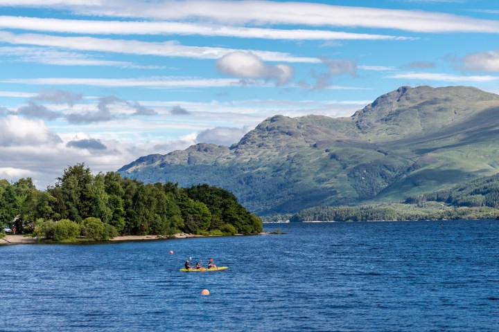 Kayakers on a lake with green hills and blue sky in the background.