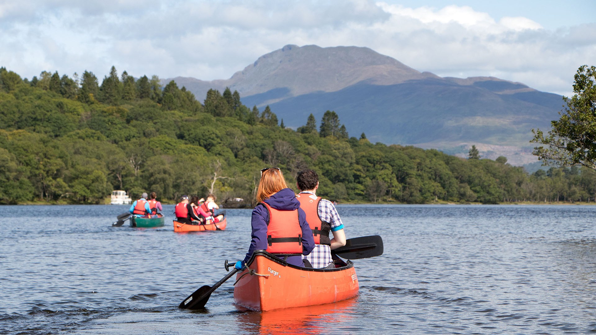 People canoeing on a lake with forested hills and mountains in the background.