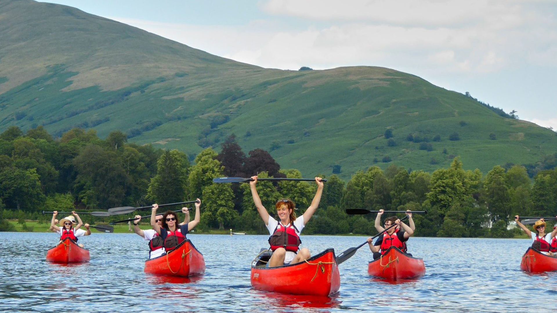 Group kayaking on a lake with green hills and trees in the background.