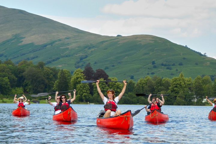 Group kayaking on a lake with green hills and trees in the background.