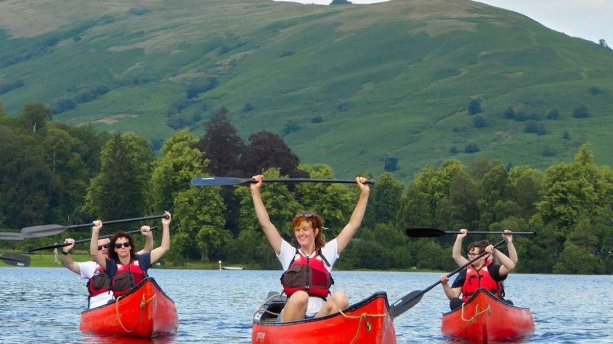 Group kayaking on a lake with green hills and trees in the background.