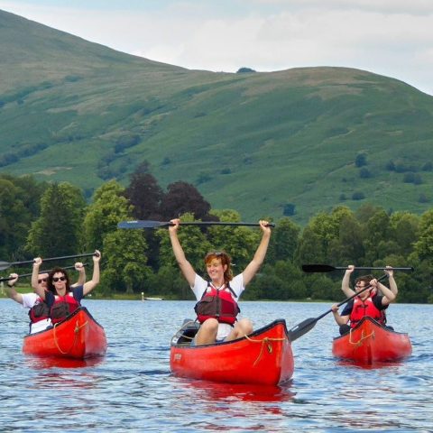 Group kayaking on a lake with green hills and trees in the background.