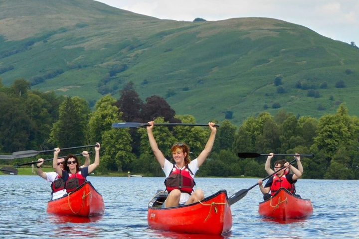 Group kayaking on a lake with green hills and trees in the background.