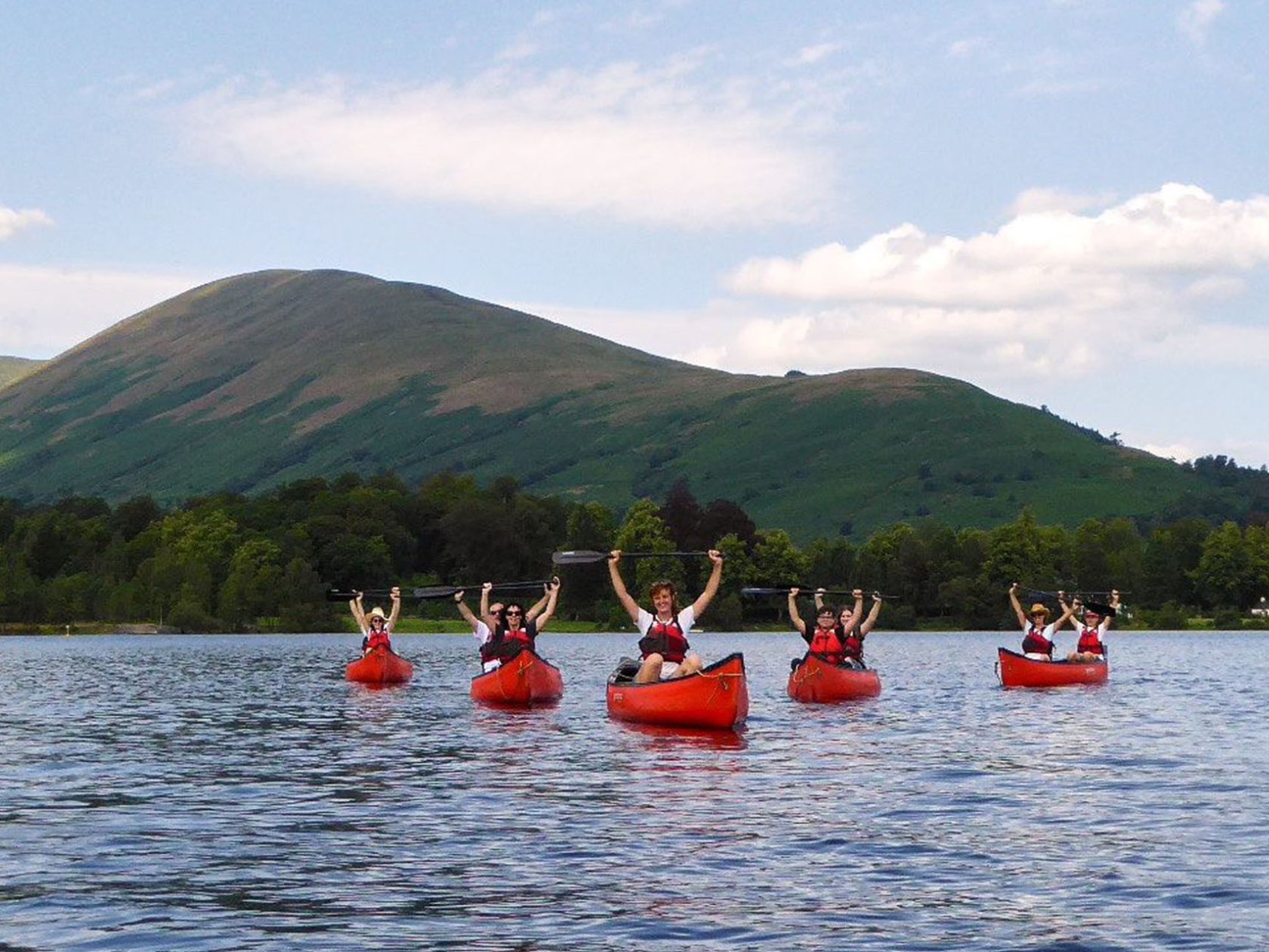 Group kayaking on a lake with green hills in the background on a sunny day.