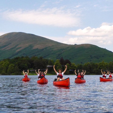 Group kayaking on a lake with green hills in the background on a sunny day.