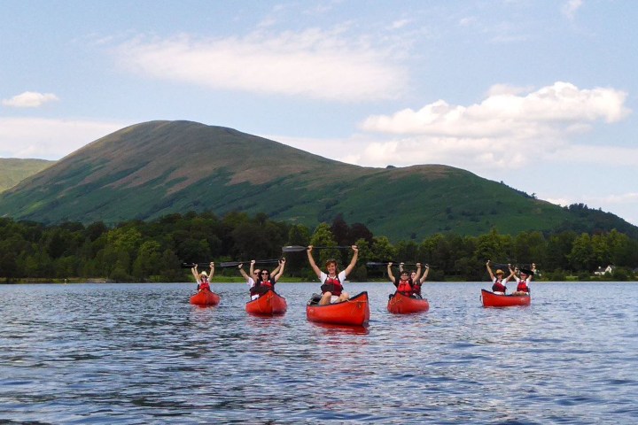 Group kayaking on a lake with green hills in the background on a sunny day.