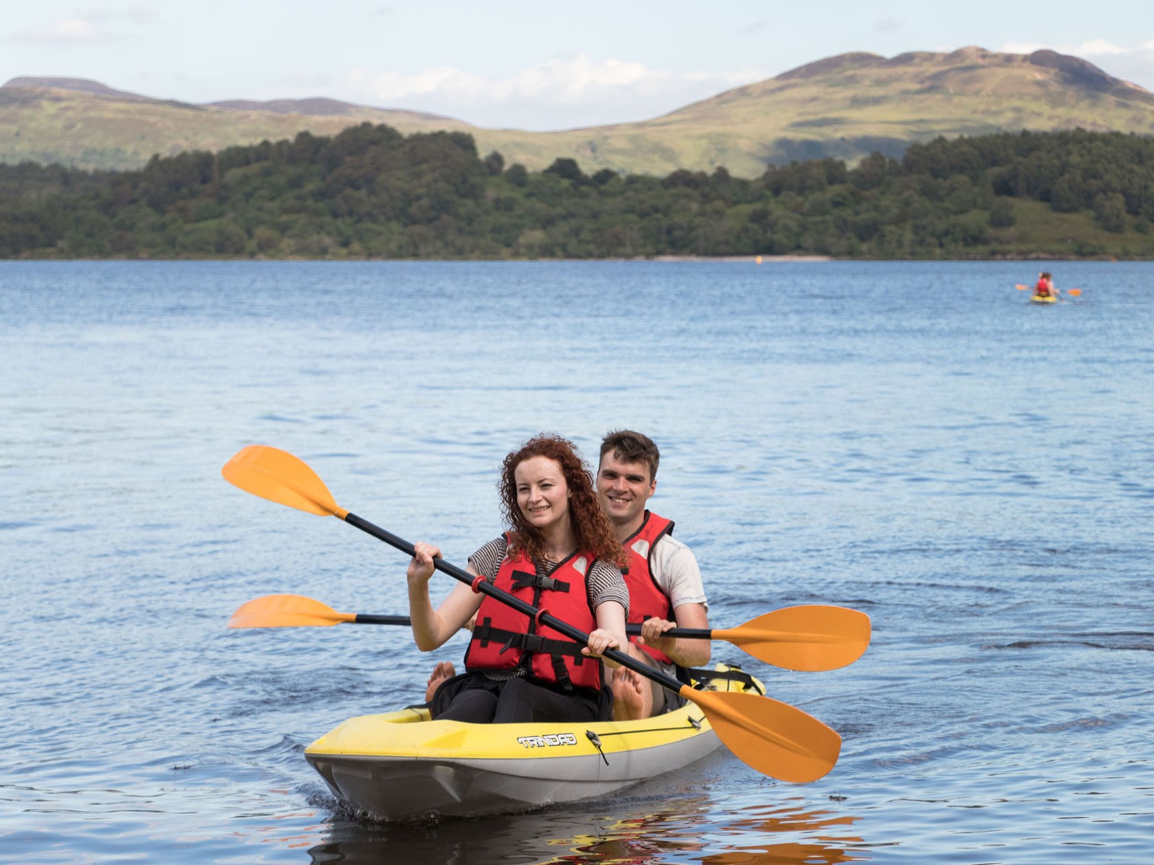 Two people kayaking on a lake with mountains in the background.