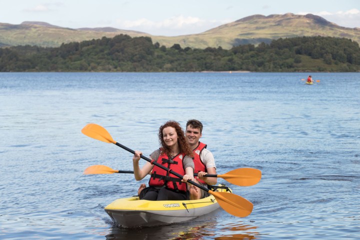 Two people kayaking on a lake with mountains in the background.