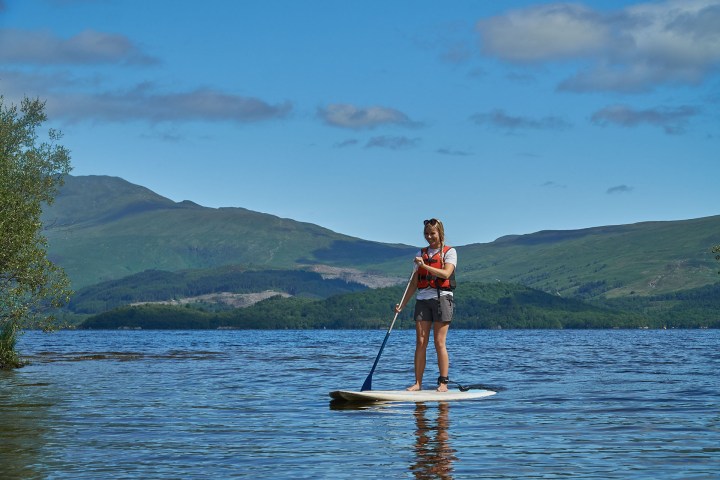 Woman paddleboarding on a lake with mountains and trees in the background.
