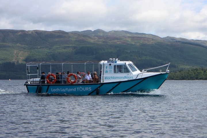 Tour boat on a lake with passengers, mountains in the background.