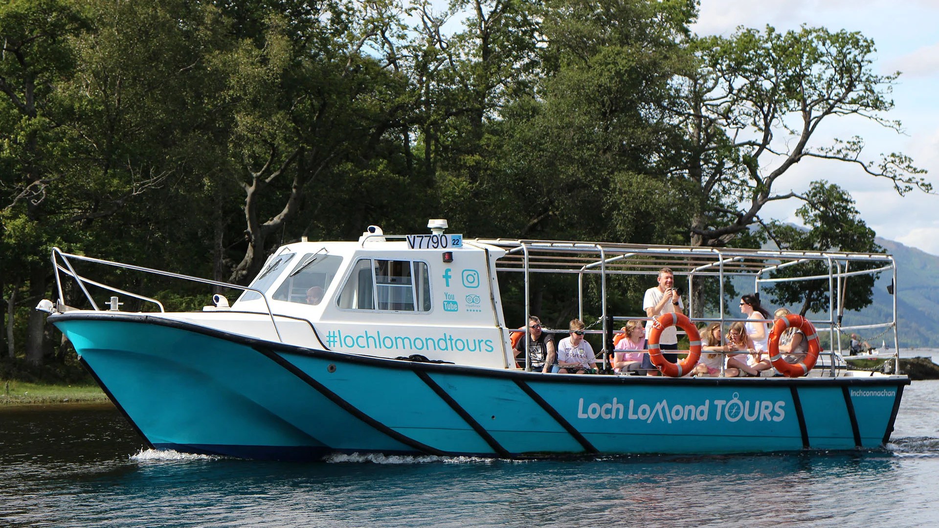 Tour boat with passengers cruising on a lake, trees in background.