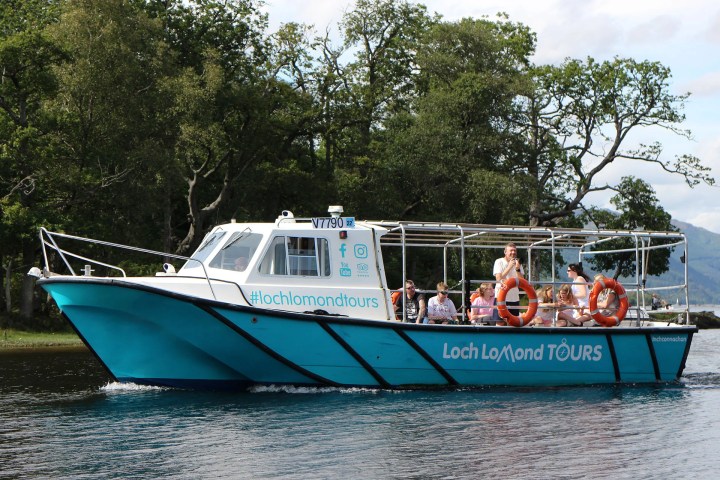 Tour boat with passengers cruising on a lake, trees in background.