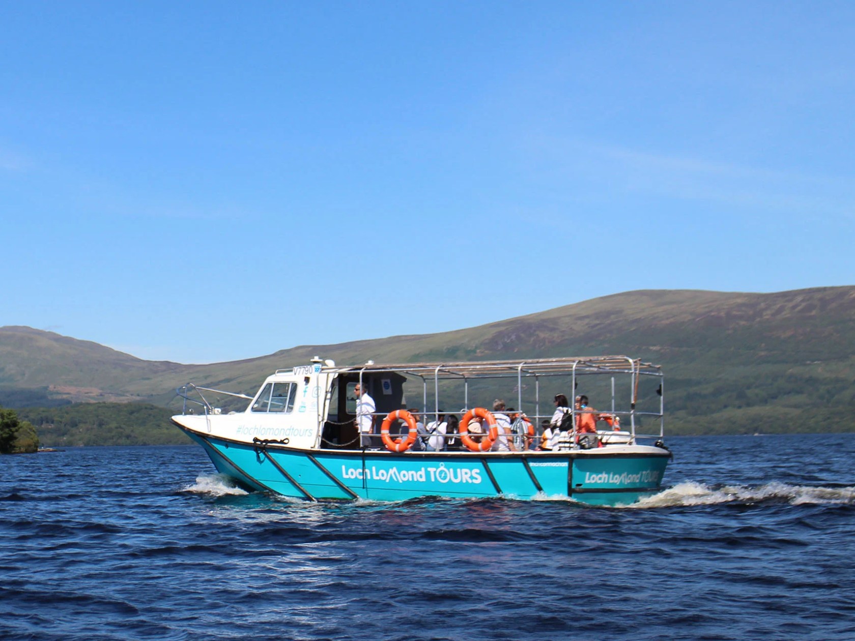 Tour boat on a lake with hills in the background under a blue sky.