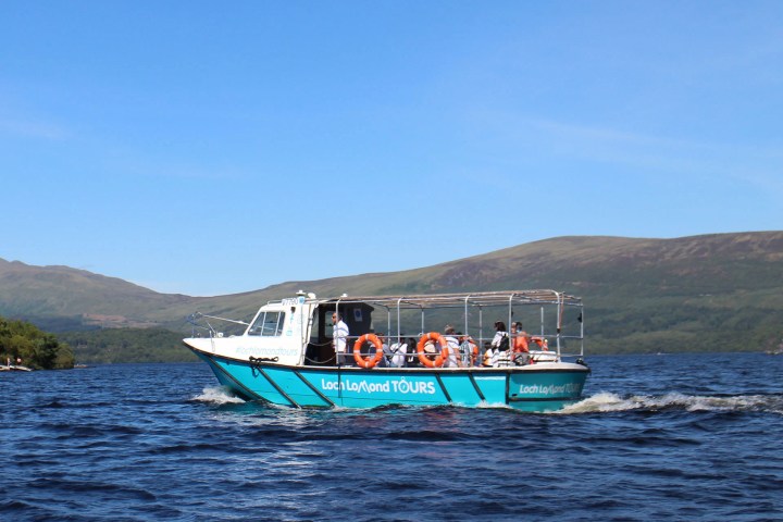 Tour boat on a lake with hills in the background under a blue sky.