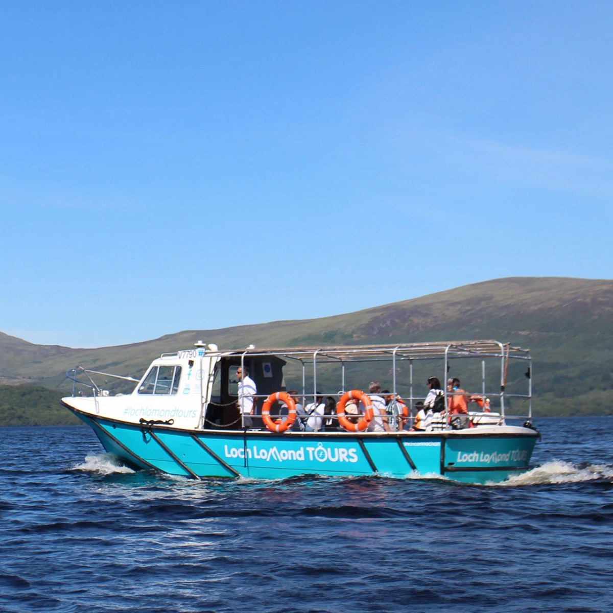 Tour boat on a lake with hills in the background under a blue sky.