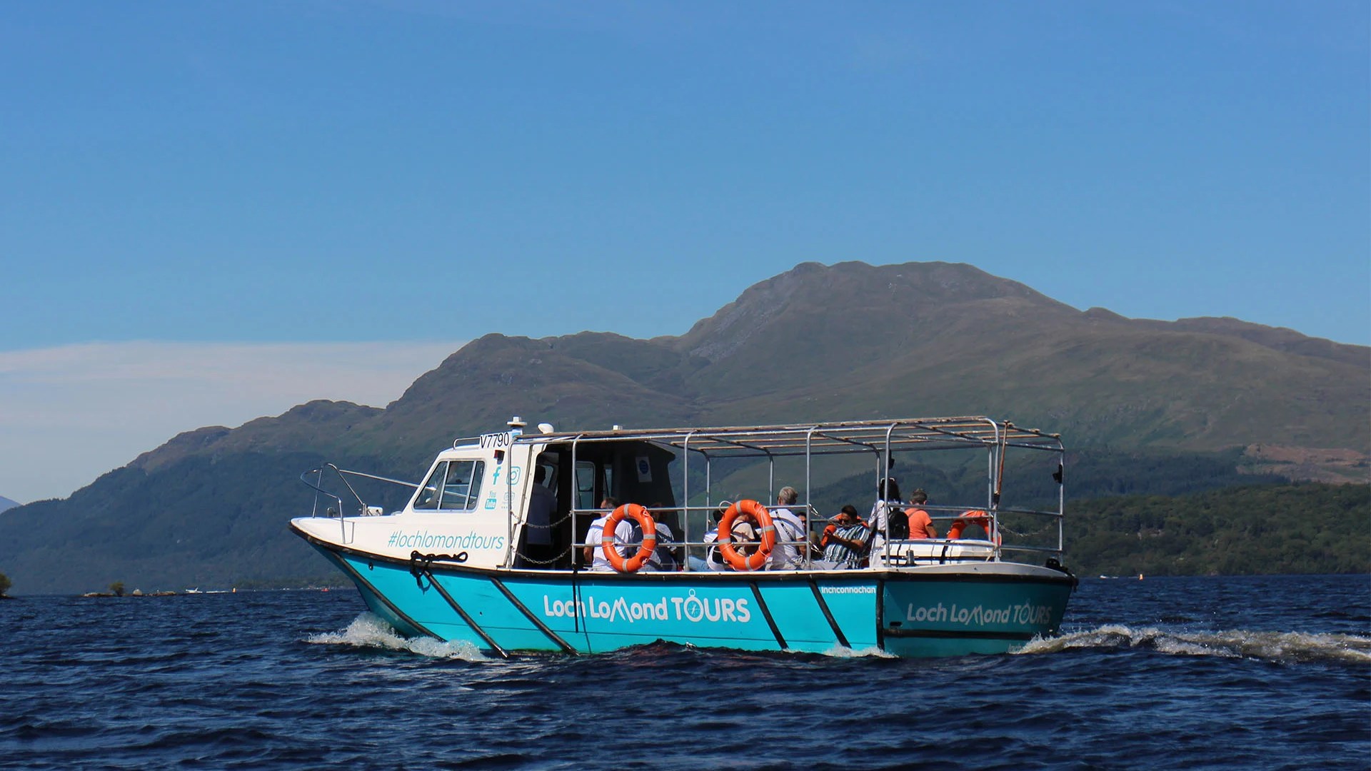 Tour boat on a lake with mountainous background under a clear blue sky.