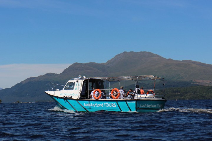 Tour boat on a lake with mountainous background under a clear blue sky.