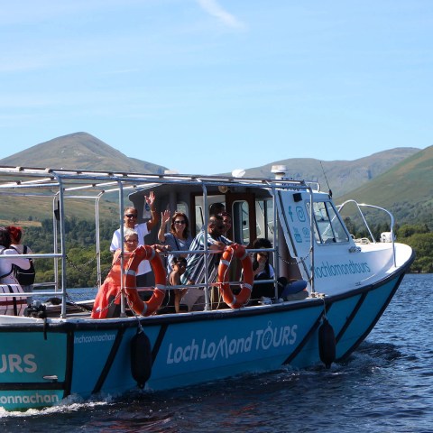 Tour boat on Loch Lomond with people enjoying the scenic landscape and hills in the background.