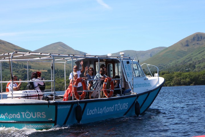 Tour boat on Loch Lomond with people enjoying the scenic landscape and hills in the background.