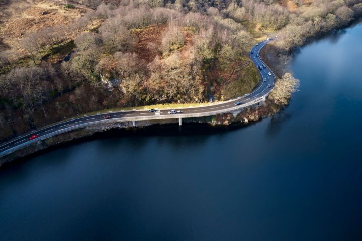 Aerial view of a winding road beside a lake, surrounded by bare trees.
