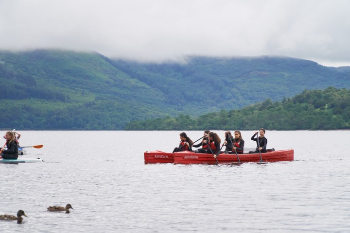 People in a red canoe paddling on a calm lake with hills in the background.