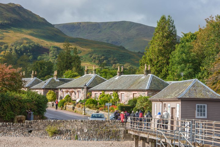 Scenic village with stone houses and mountains in the background under a cloudy sky.