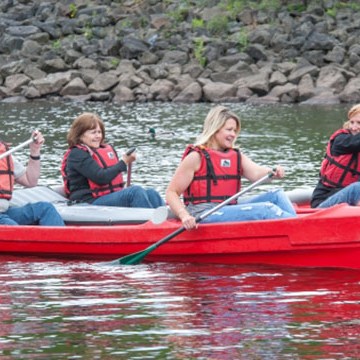 Four people in red canoe paddling on a calm river.